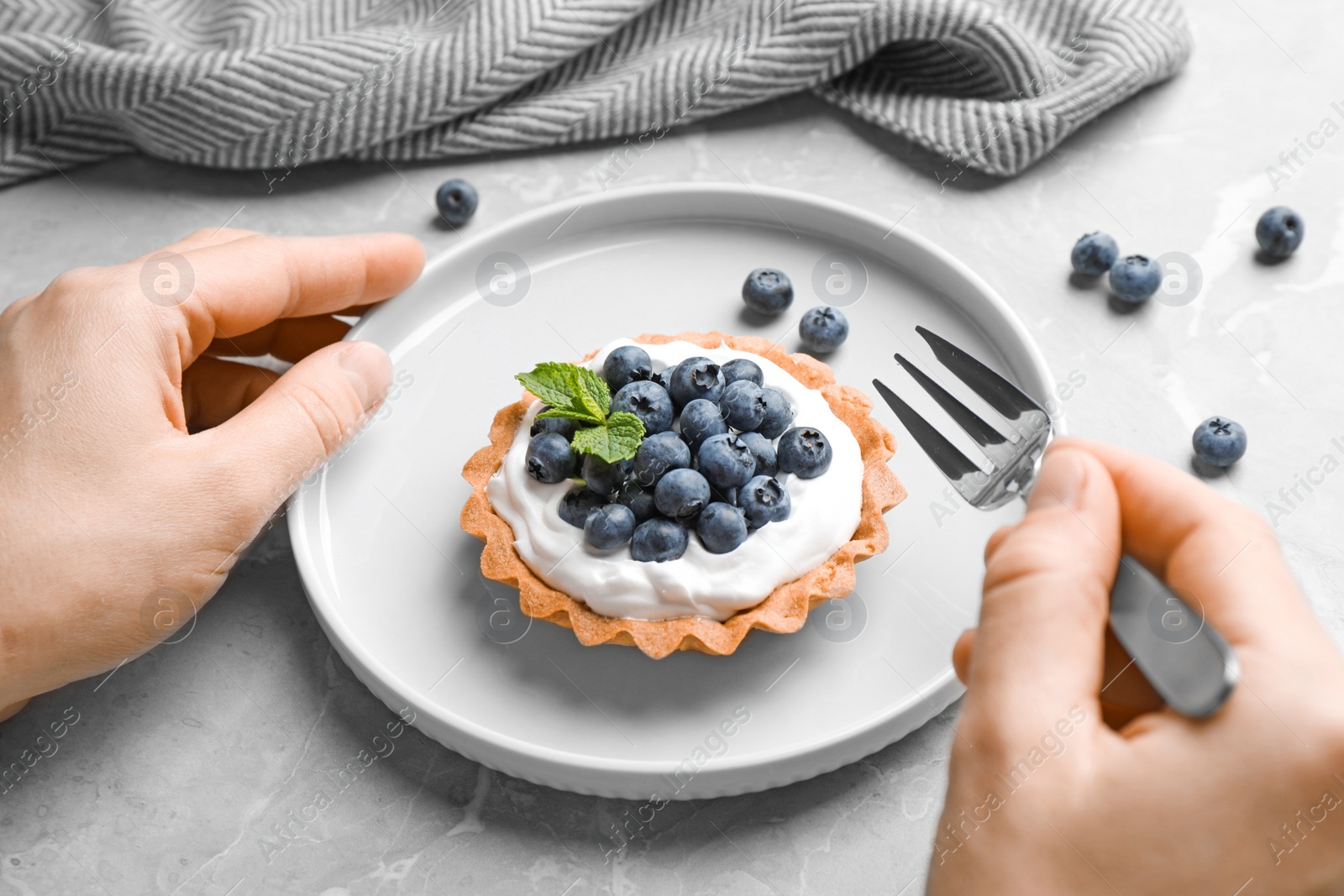 Photo of Woman eating blueberry tart at marble table, closeup. Delicious pastries