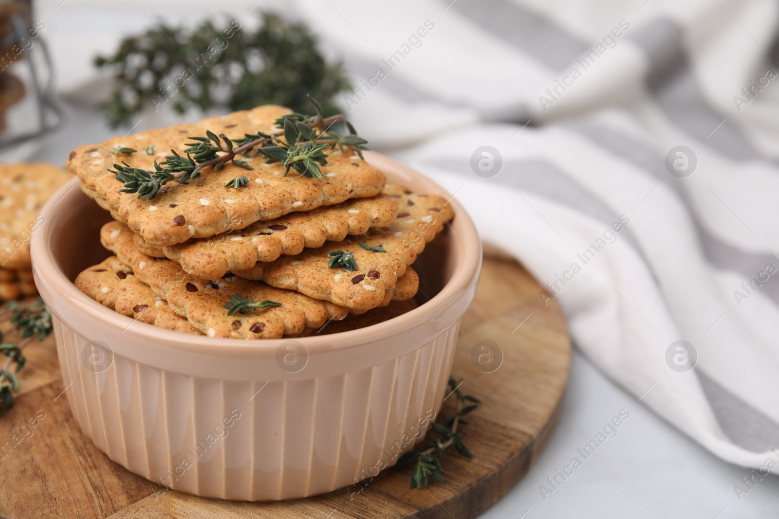 Photo of Cereal crackers with flax, sesame seeds and thyme in bowl on light table, closeup. Space for text