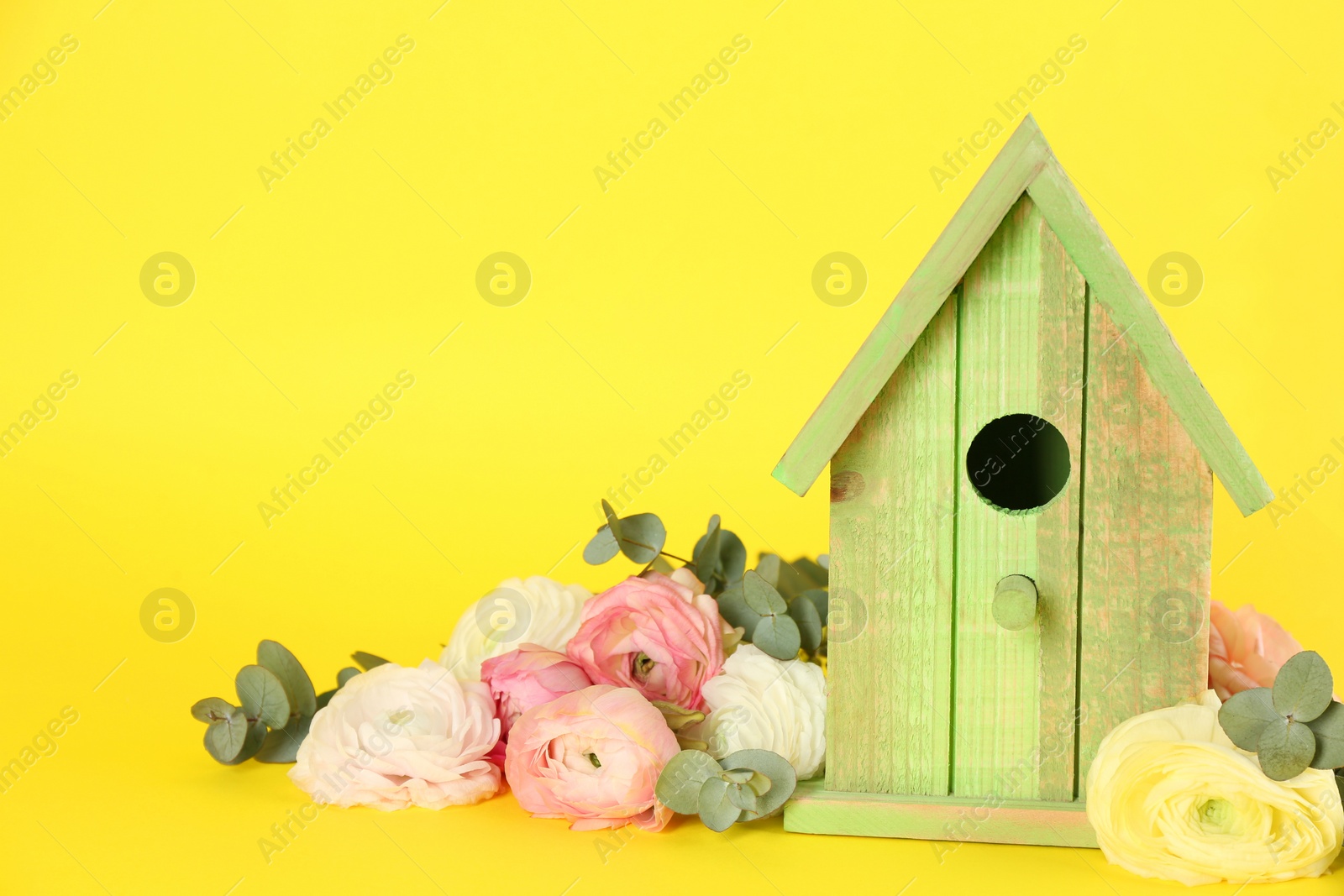 Photo of Stylish bird house and fresh eustomas on yellow background. Space for text