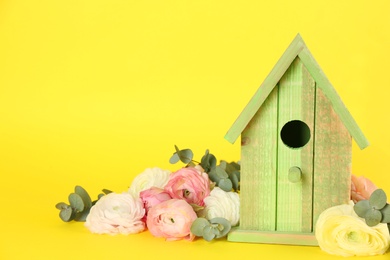 Stylish bird house and fresh eustomas on yellow background. Space for text