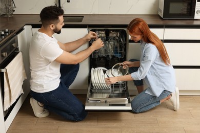 Photo of Lovely couple loading dishwasher with plates in kitchen