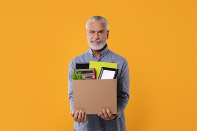Photo of Confused unemployed senior man with box of personal office belongings on orange background