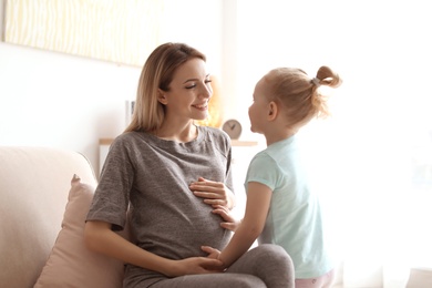 Young pregnant woman with cute daughter at home