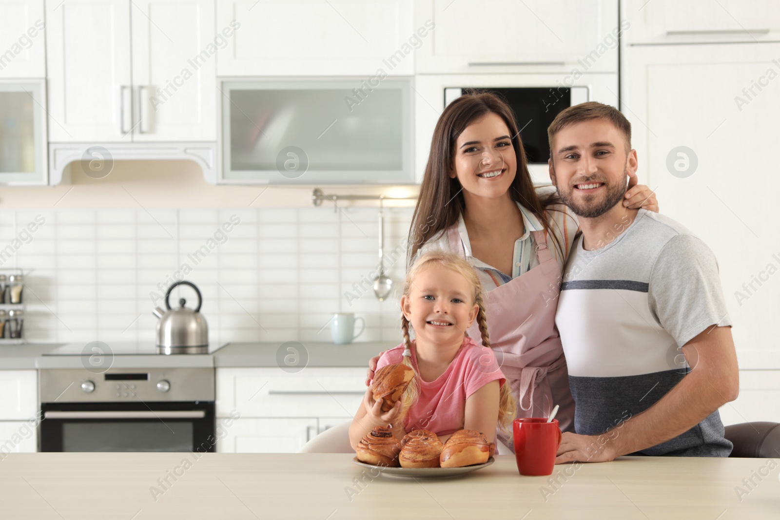 Photo of Happy family with freshly oven baked buns at table in kitchen. Space for text