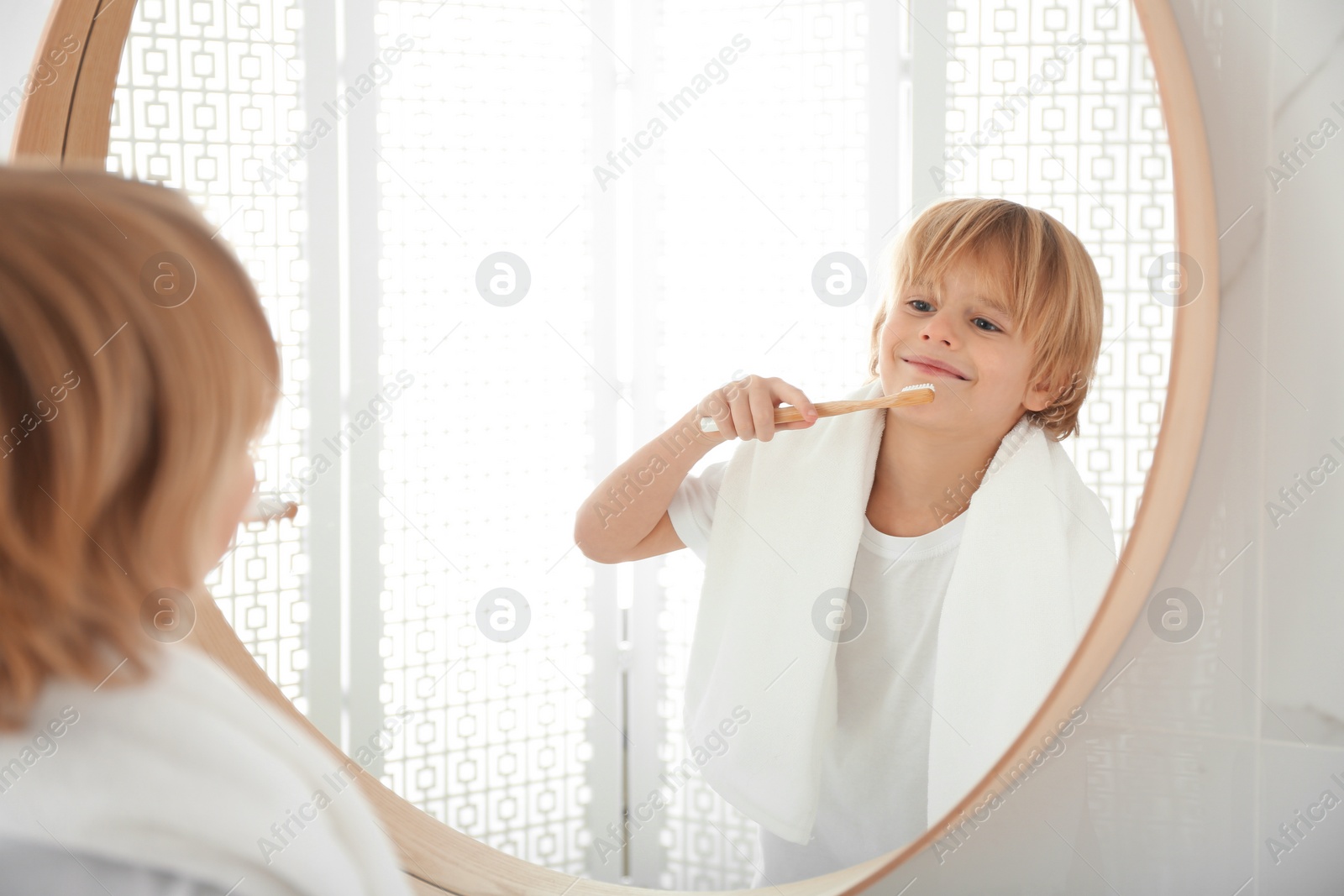 Photo of Cute little boy brushing teeth near mirror in bathroom