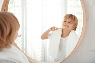 Cute little boy brushing teeth near mirror in bathroom