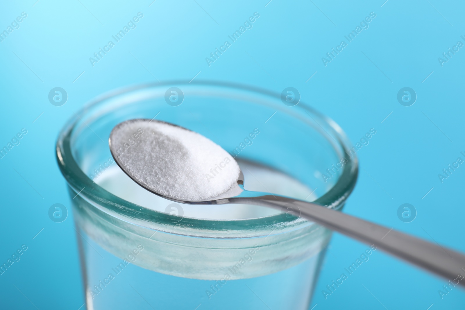 Photo of Spoon with baking soda over glass of water on light blue background, closeup