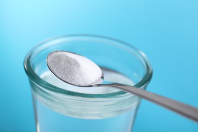 Spoon with baking soda over glass of water on light blue background, closeup