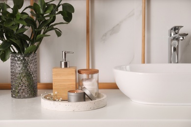 Photo of Vase with green branches, soap dispenser and cotton pads near vessel sink in bathroom