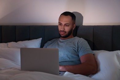 Photo of Young man using laptop in bed at night. Internet addiction