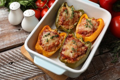 Photo of Tasty stuffed peppers in dish and ingredients on wooden table