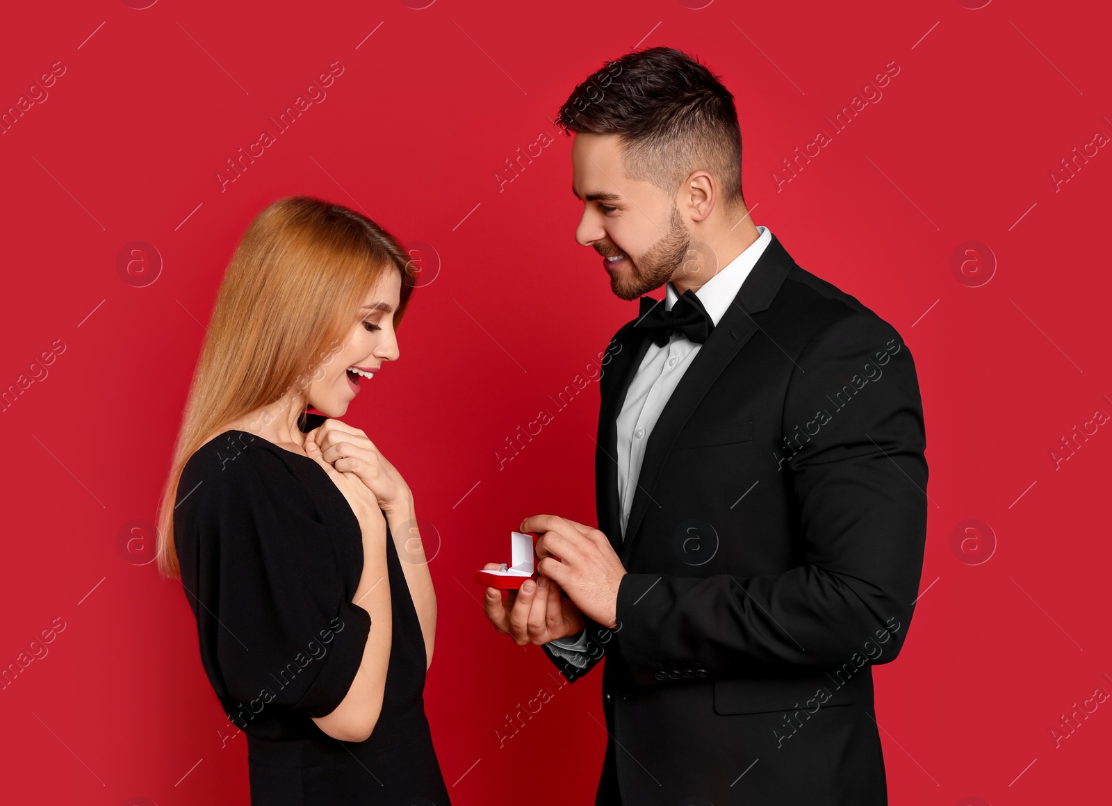 Photo of Man with engagement ring making marriage proposal to girlfriend on red background