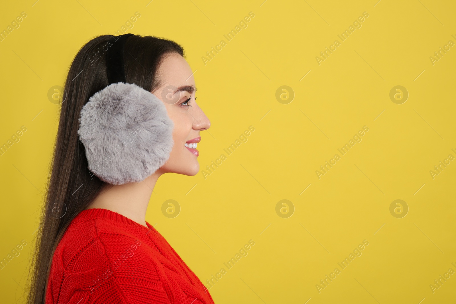 Photo of Beautiful young woman wearing earmuffs on yellow background. Space for text