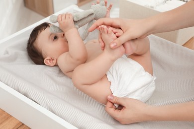 Mother changing baby's diaper on table at home, closeup