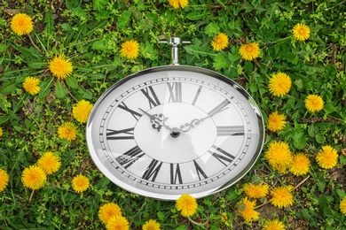 Retro clock on green grass with dandelions, outdoors. Time change concept