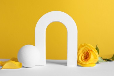 Photo of Beautiful presentation for product. Geometric figures and rose on white table against yellow background