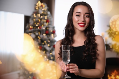 Photo of Beautiful woman in elegant black dress with glass of champagne at home. Christmas celebration