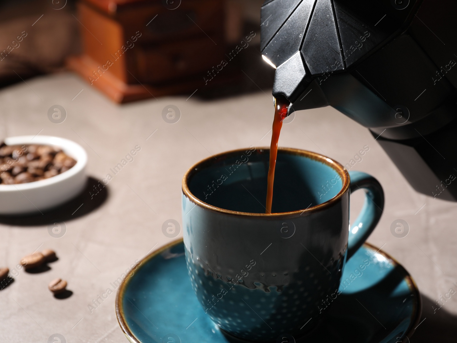 Photo of Pouring aromatic coffee from moka pot into cup at light table, closeup