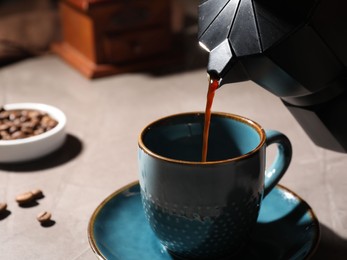 Pouring aromatic coffee from moka pot into cup at light table, closeup