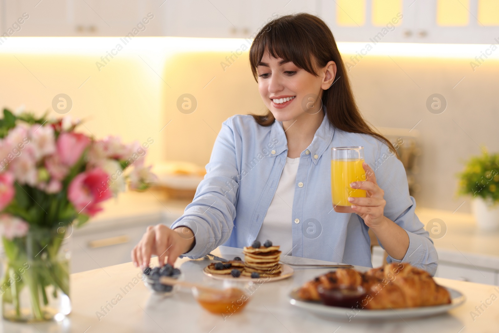 Photo of Smiling woman with glass of juice having breakfast at home