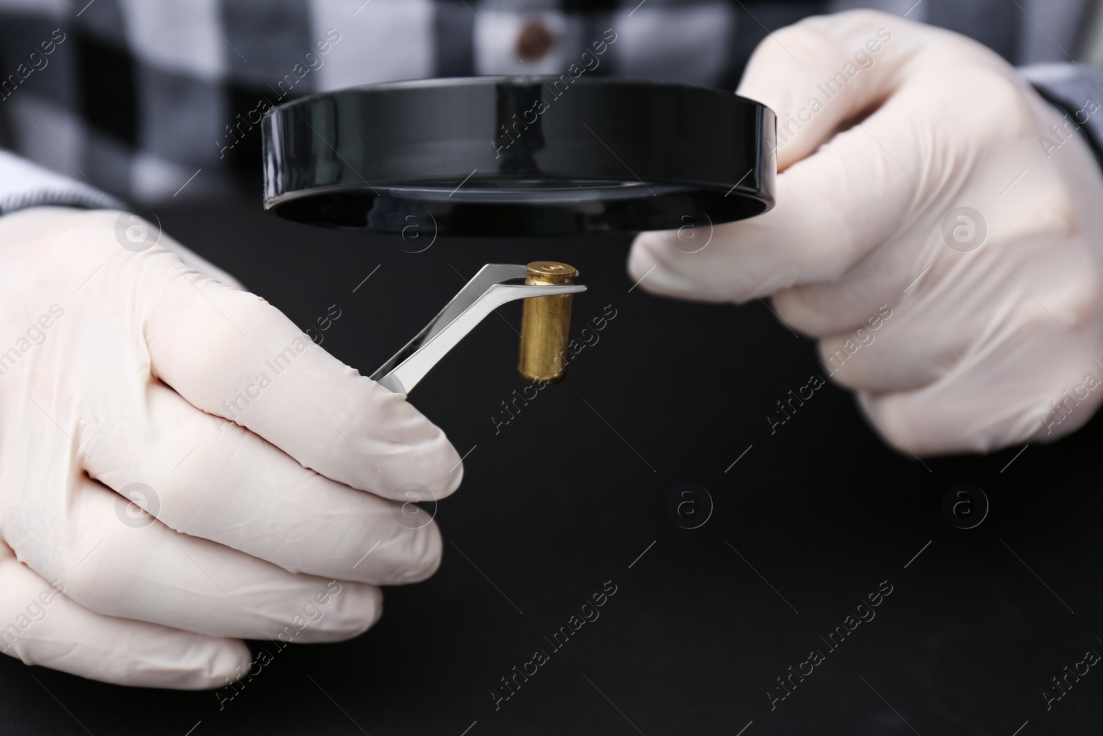 Photo of Detective exploring bullet shell with magnifying glass on black background, closeup