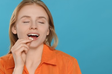 Woman putting bubble gum into mouth on light blue background. Space for text