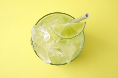 Photo of Glass of refreshing drink with lime on yellow background, top view