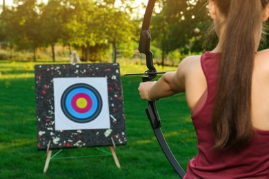 Photo of Woman with bow and arrow aiming at archery target in park, back view