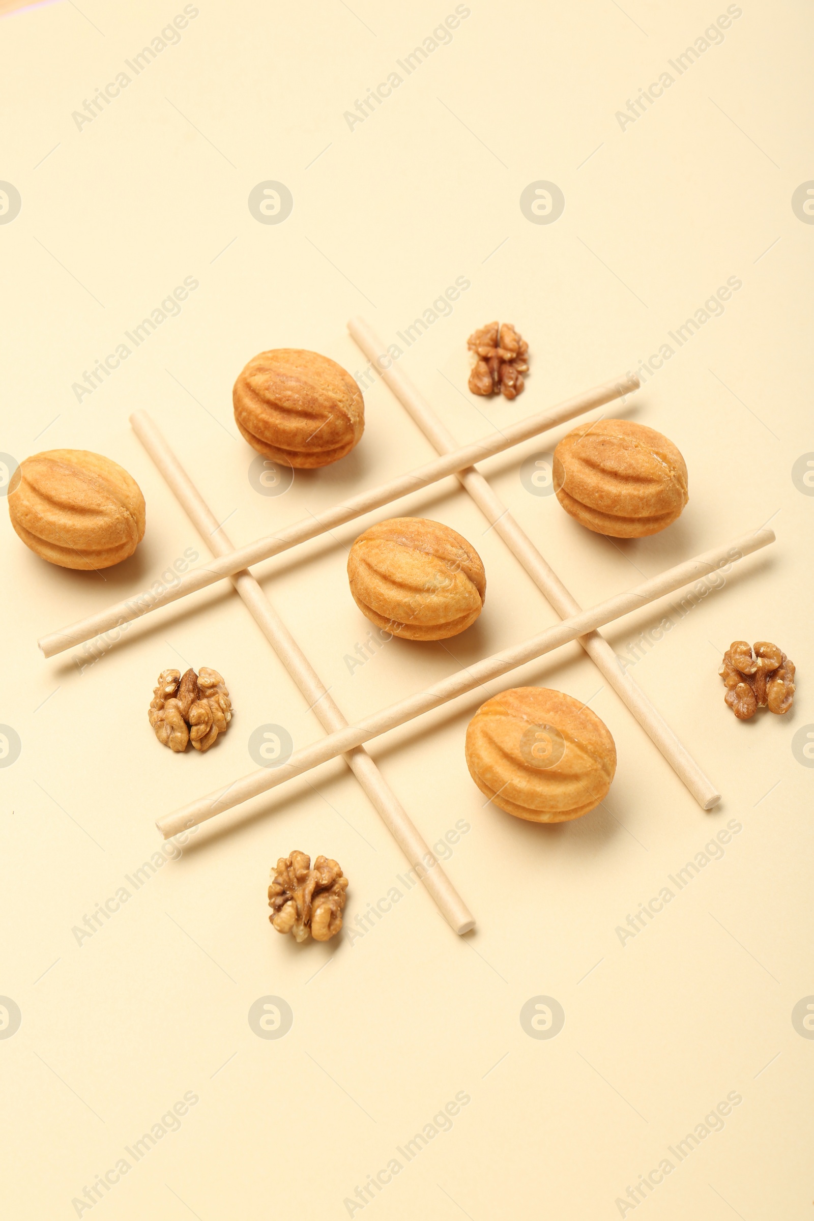 Photo of Tic tac toe game made with walnuts and cookies on beige background