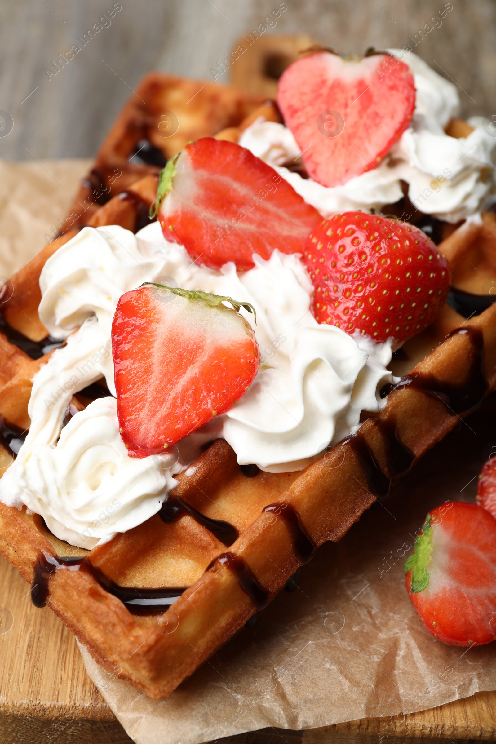Photo of Delicious Belgian waffles with strawberry, whipped cream and chocolate sauce on board, closeup