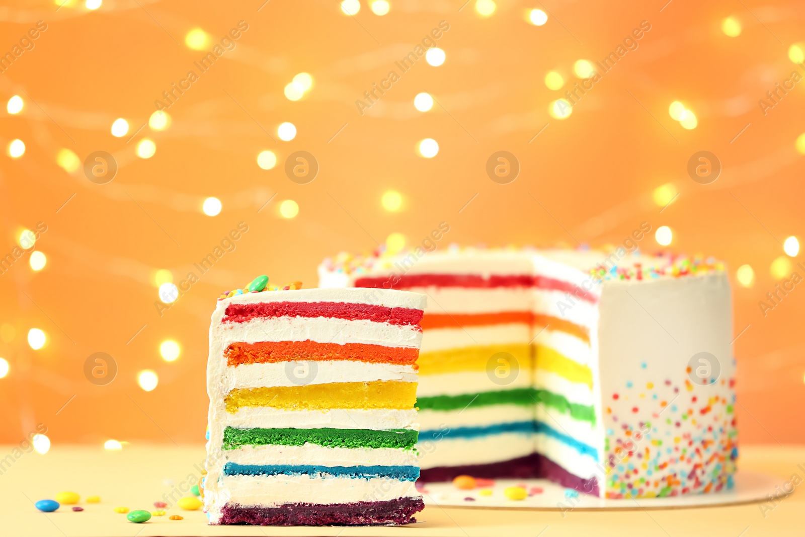 Photo of Delicious rainbow cake on table against blurred lights