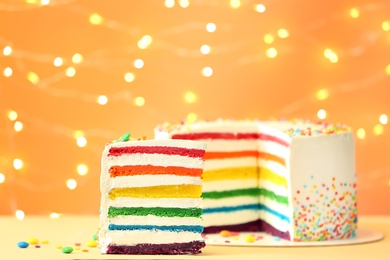 Photo of Delicious rainbow cake on table against blurred lights