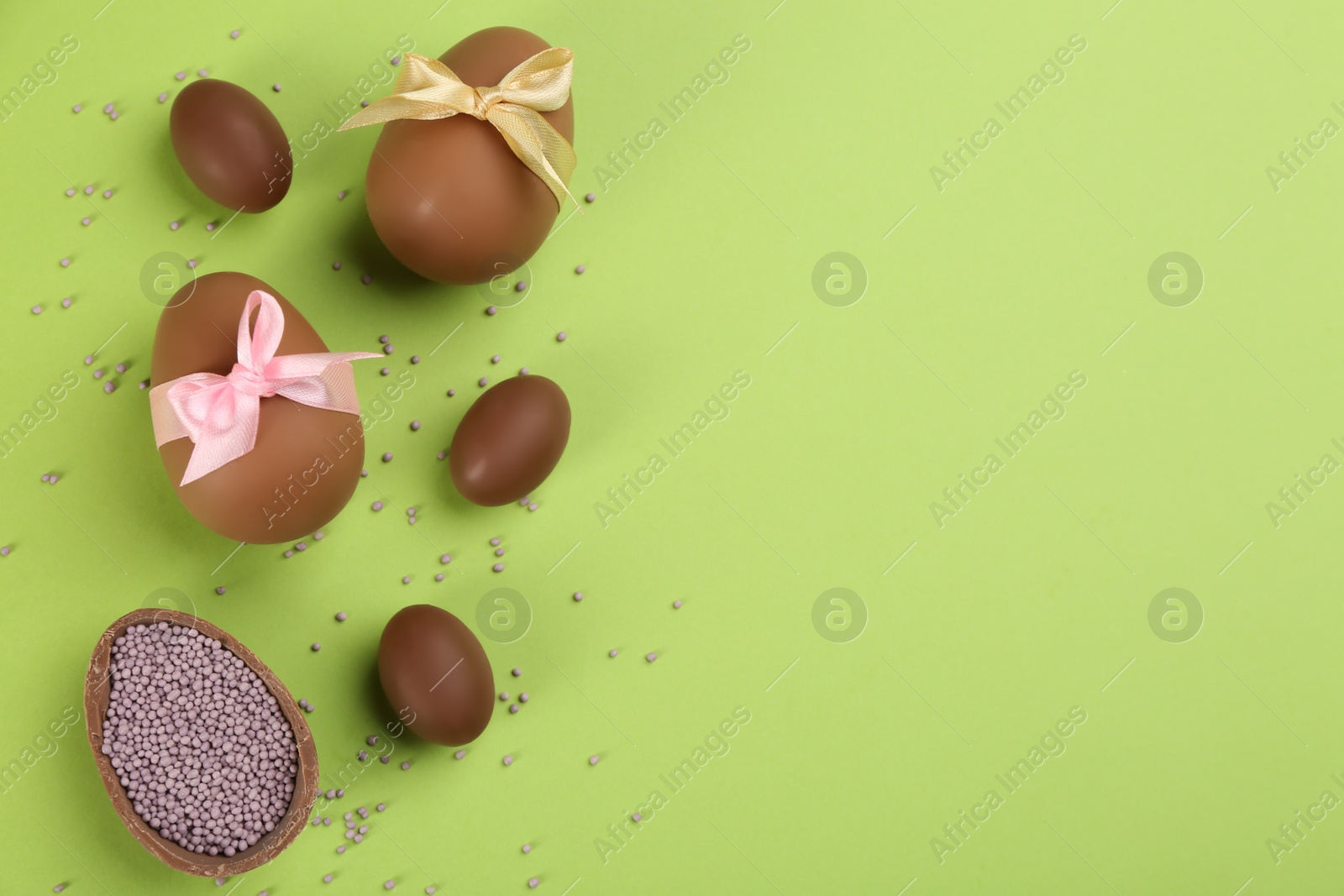 Photo of Sweet chocolate eggs on light green background, flat lay. Space for text