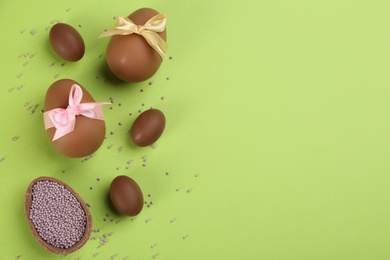 Sweet chocolate eggs on light green background, flat lay. Space for text