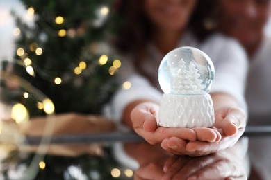 Happy couple celebrating Christmas, focus on hands with snow globe