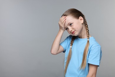 Photo of Little girl suffering from headache on grey background. Space for text