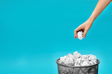 Woman throwing crumpled paper into metal bin on color background, closeup. Space for text