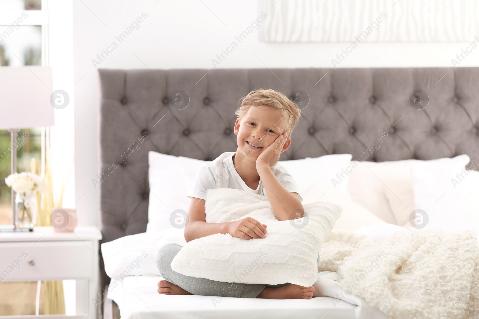 Photo of Cute little boy with pillow sitting on bed at home