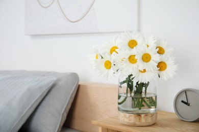 Photo of Bouquet of beautiful daisy flowers and clock on wooden table in bedroom, space for text