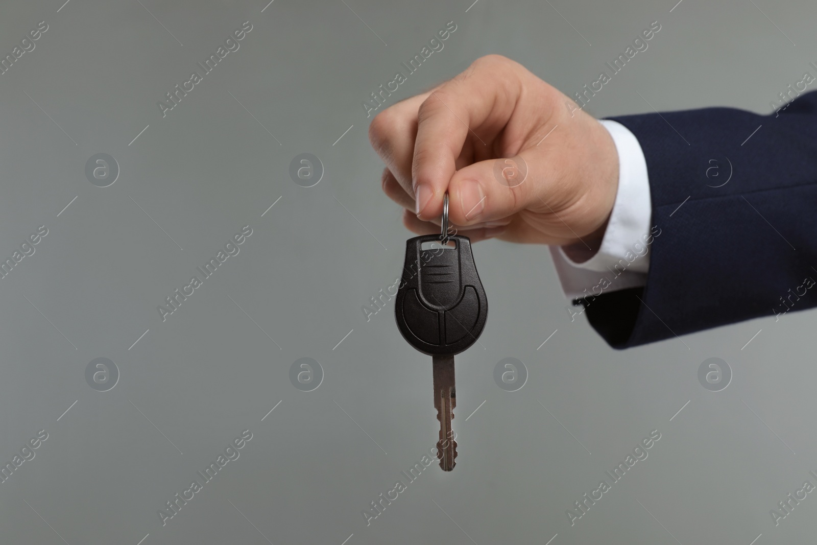 Photo of Young man holding car key on grey background, closeup. Space for text