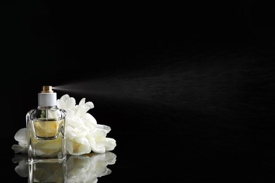 Spraying bottle of perfume and flowers on black background