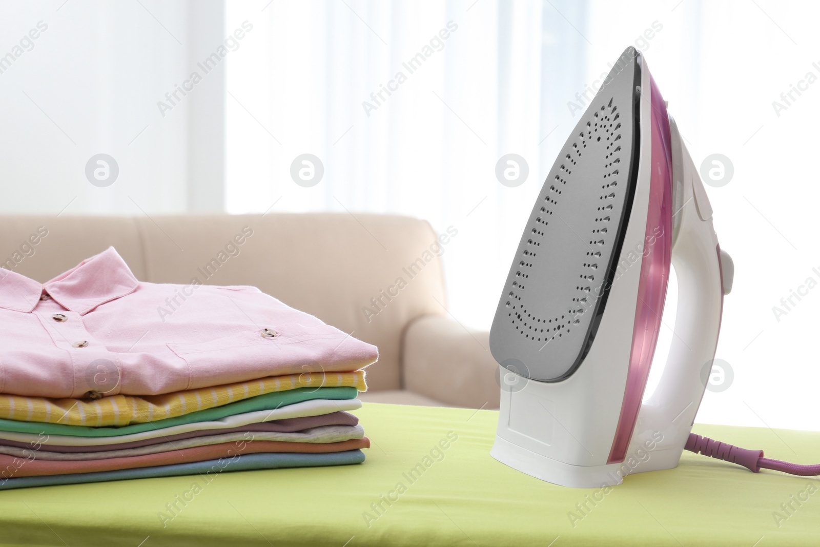 Photo of Board with modern iron and clean laundry at home