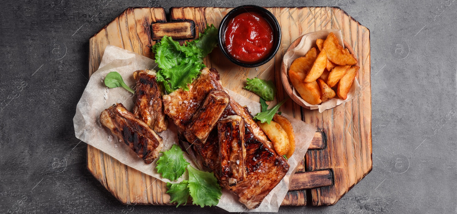 Image of Delicious grilled ribs and garnish on grey table, top view. Banner design