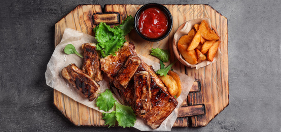 Image of Delicious grilled ribs and garnish on grey table, top view. Banner design