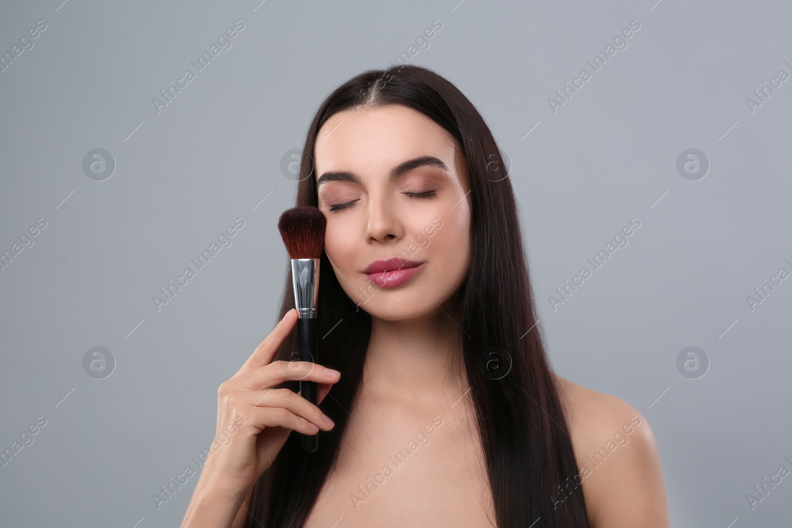 Photo of Beautiful woman with makeup brush on light grey background