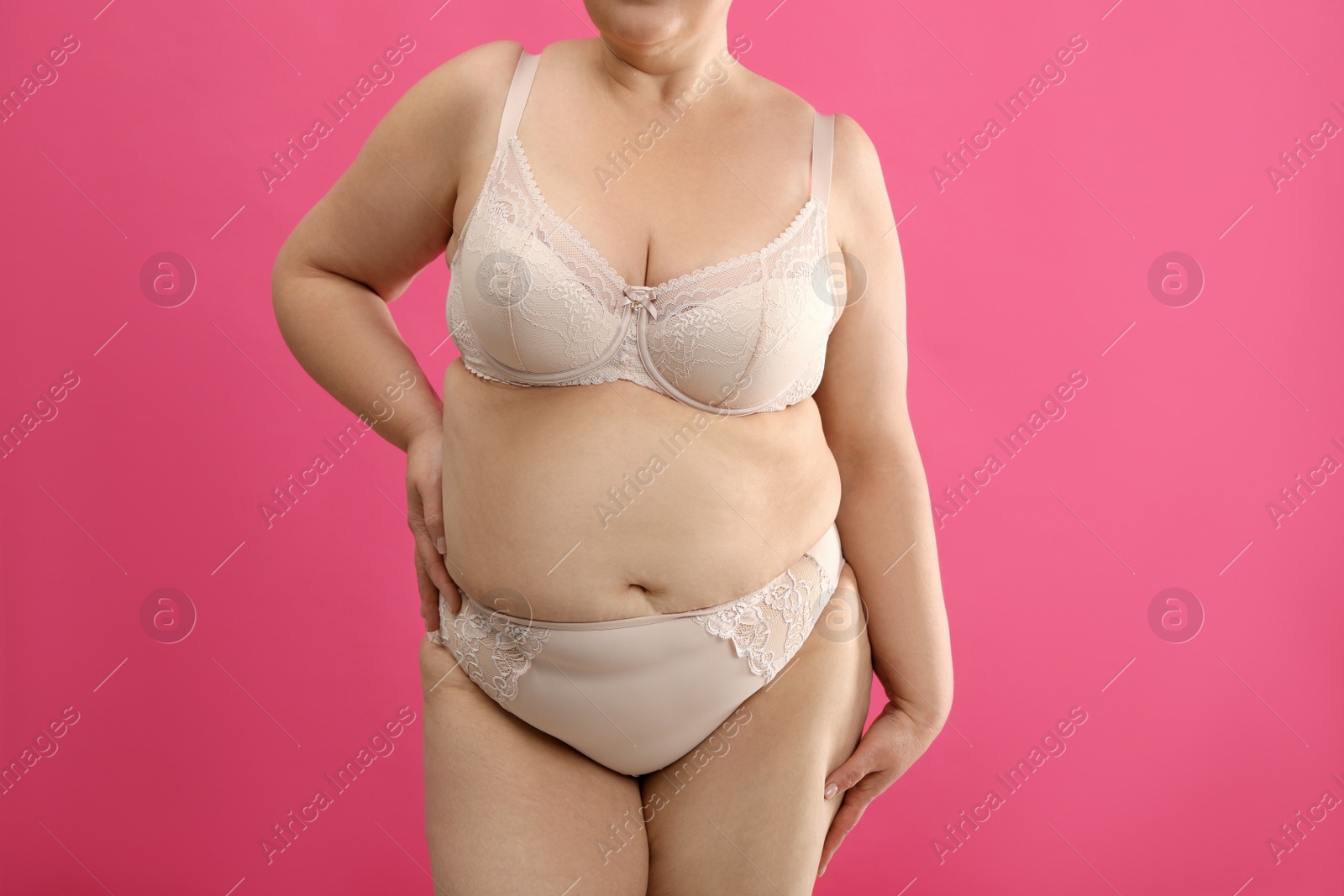 Photo of Overweight woman in beige underwear on pink background, closeup. Plus-size model