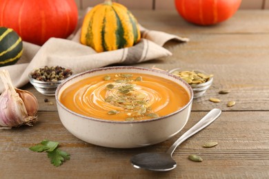 Photo of Bowl of delicious pumpkin soup with seeds and cream served on wooden table