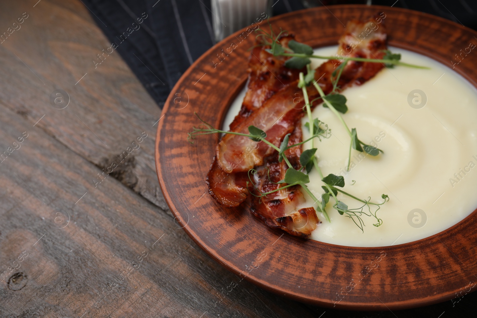 Photo of Delicious potato soup with bacon and microgreens in bowl on wooden table, closeup. Space for text