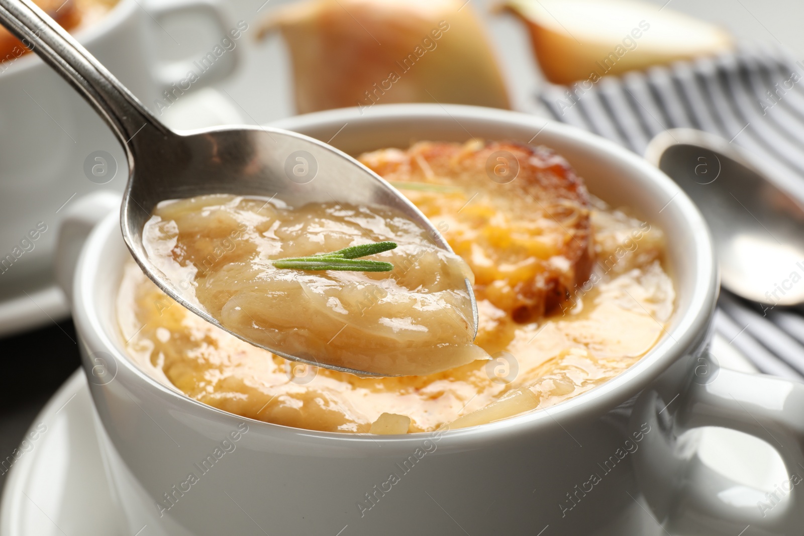 Photo of Spoon with fresh homemade homemade french onion soup over bowl, closeup
