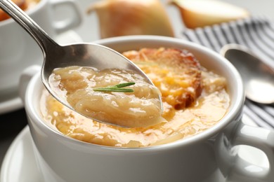 Spoon with fresh homemade homemade french onion soup over bowl, closeup